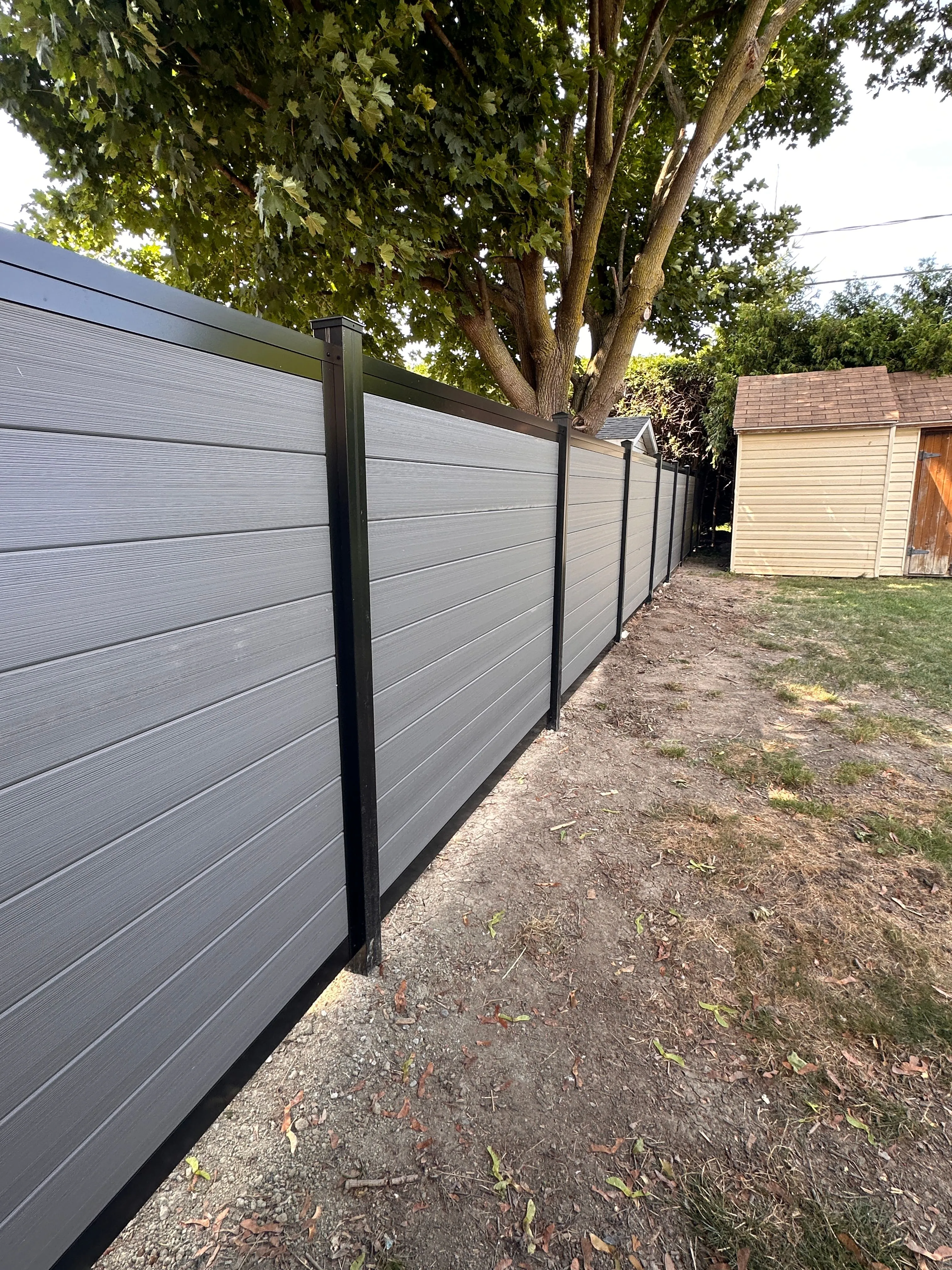 Clôture en composite gris le long d'une cour arrière avec cabanon